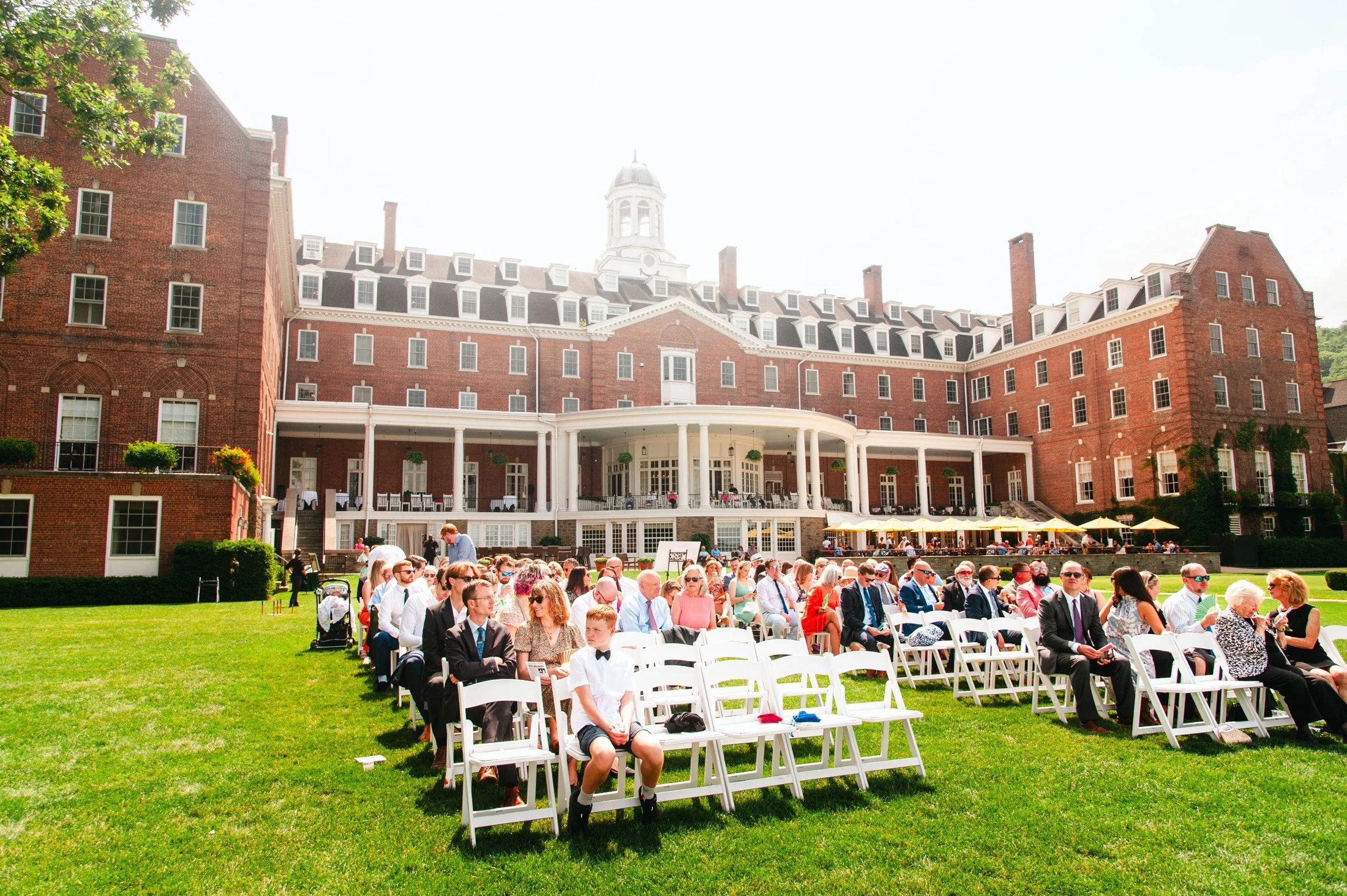The Otesaga Resort Hotel above guests seated for Amanda and Chris’s outdoor wedding ceremony in Cooperstown