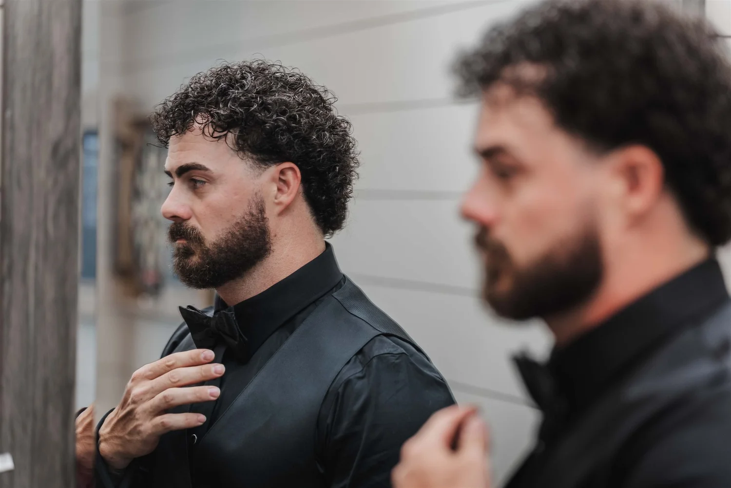 Josh adjusts his black bow tie, seen in a mirror in the getting-ready room.