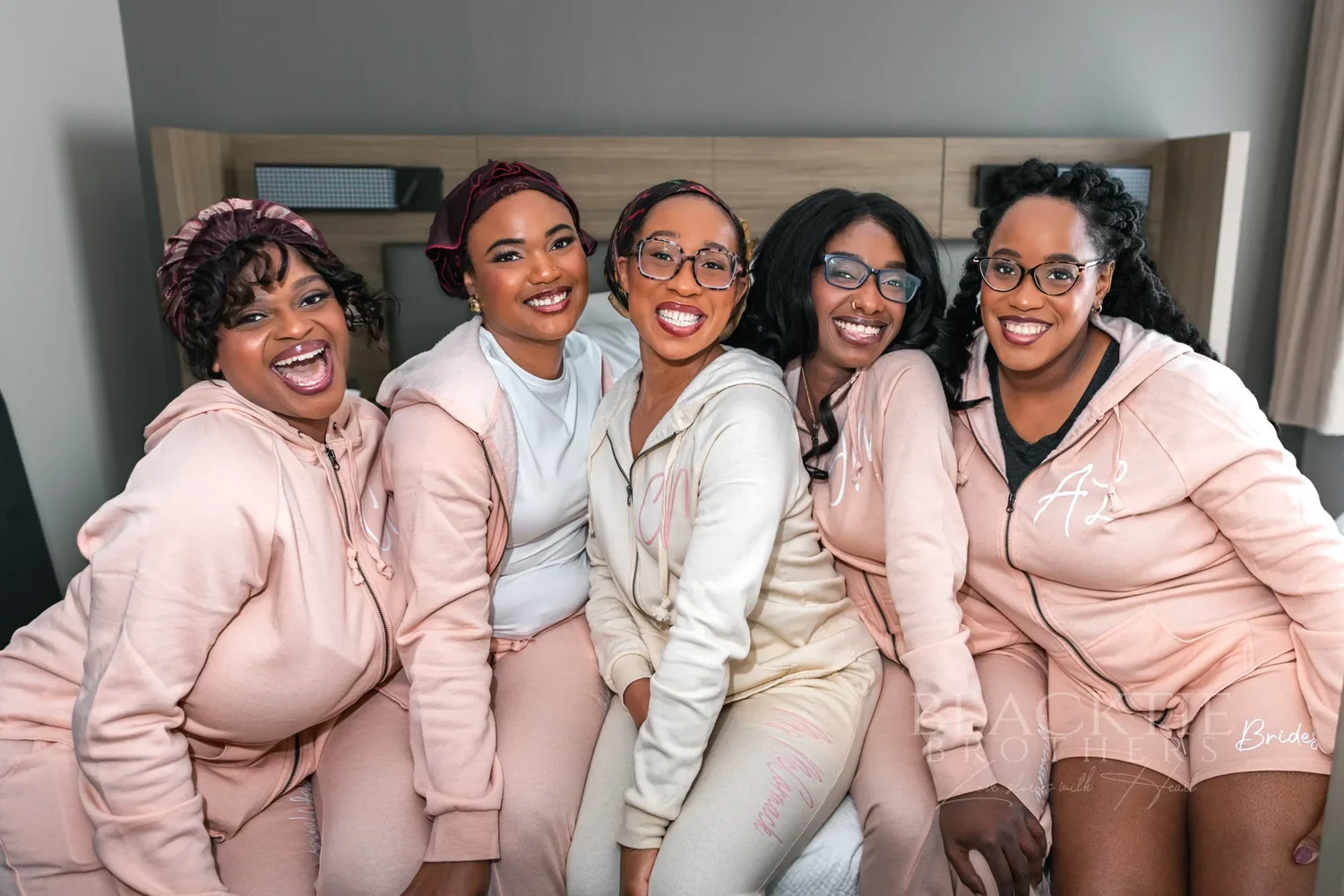 Five bridesmaids in matching pink loungewear leaning together and smiling while getting ready