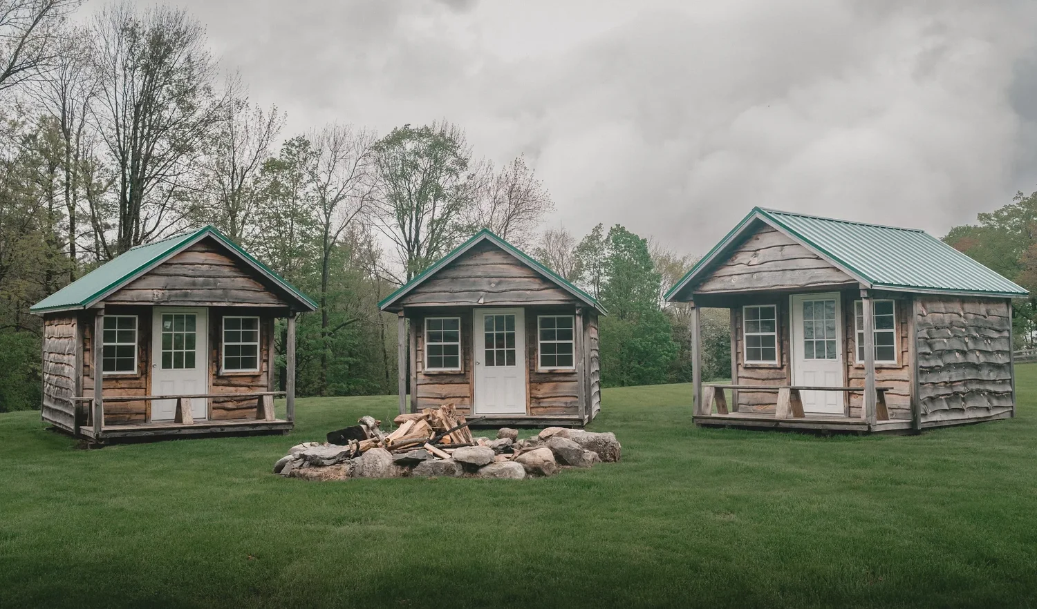 Three small wooden bungalows with green roofs around a stone fire pit at Knotting Hill Farm