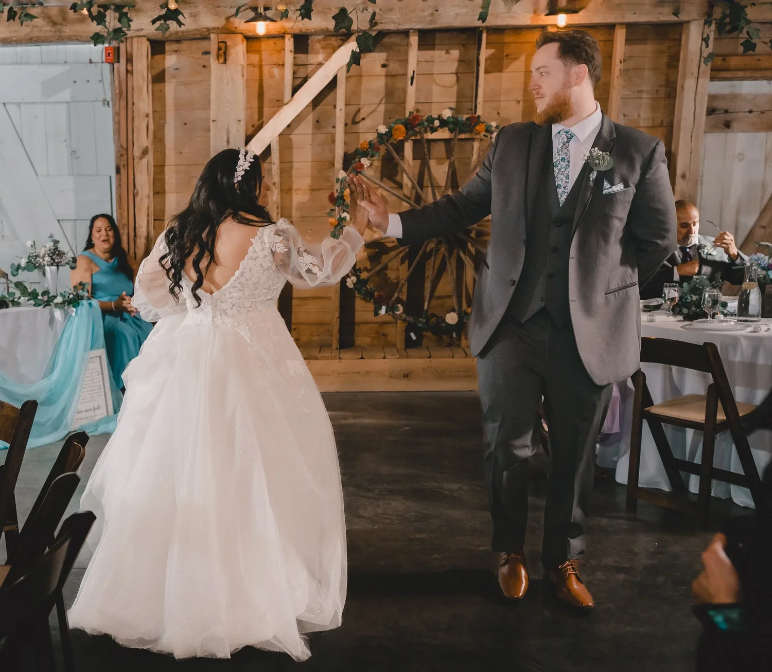 Jessica twirling under Christian’s arm during their first dance in the Grand Barn Hall, with a wagon wheel on the wall behind them