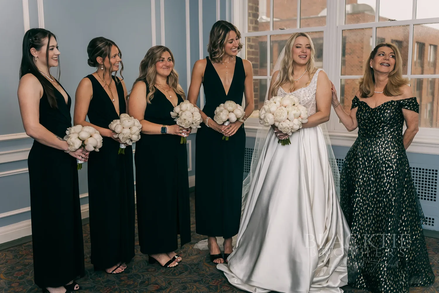 Catie with her bridesmaids in black gowns in a blue-paneled room at Marriott Syracuse Downtown