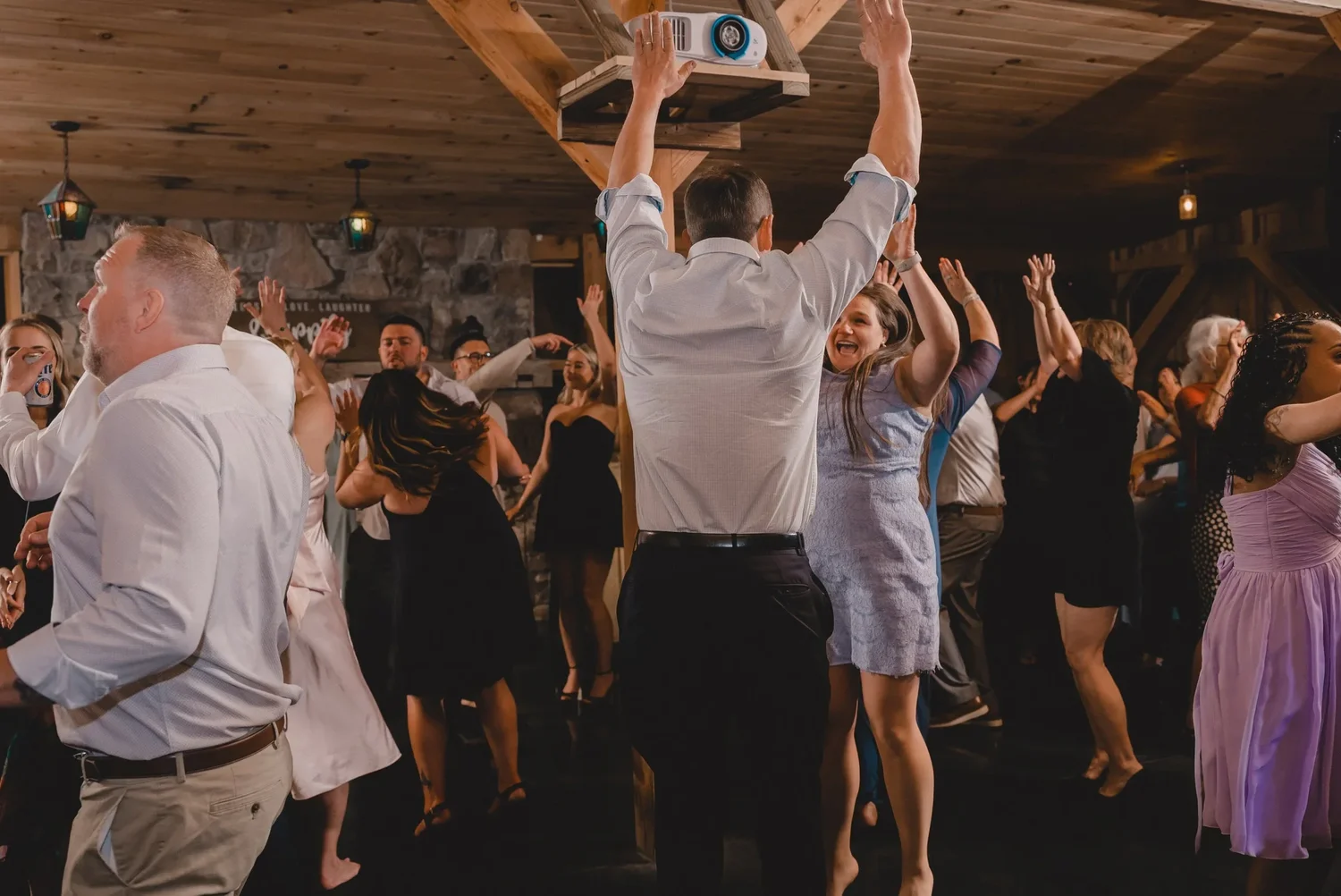 Guests dancing with their arms raised under the timber beams of the Grand Barn Hall