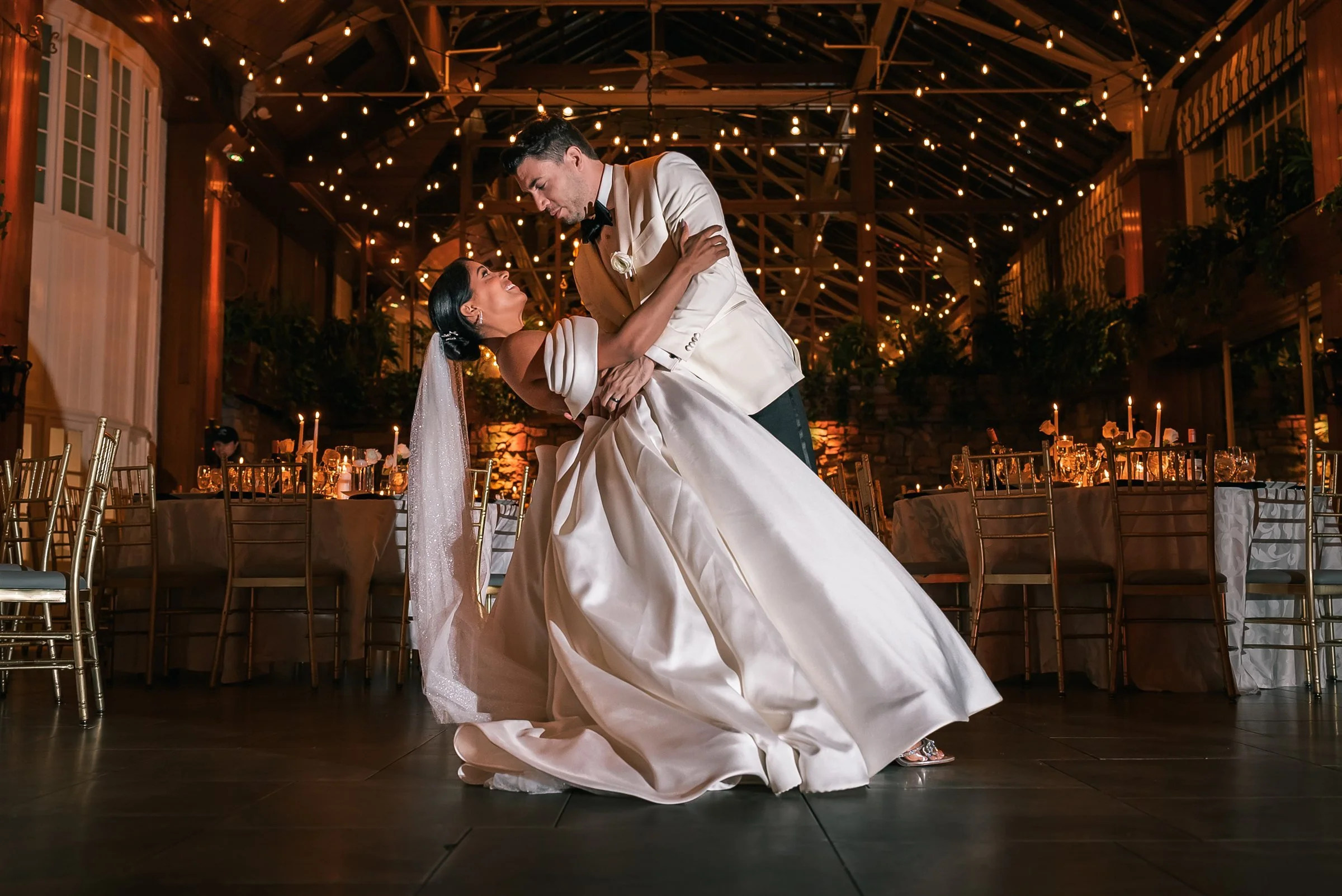 Joshua dips Patricia beneath strings of lights in The Somerley reception room at Fox Hollow.