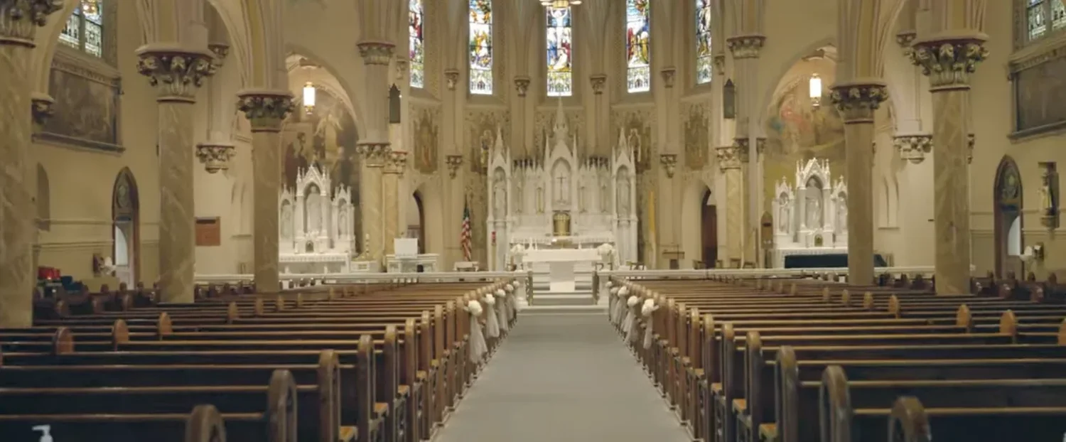 The empty nave of St. Mary's Church in Clinton, pews tied with white ribbon and flowers, the white altar and stained glass at the far end