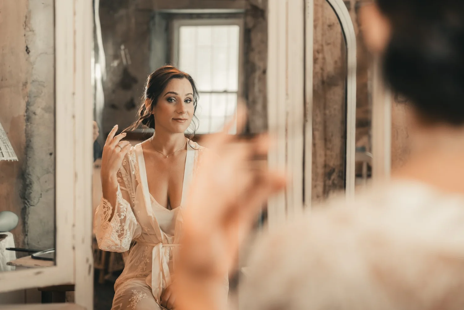 Jill looking into an antique mirror while getting ready in a room with exposed stone walls at The Sinclair of Skaneateles