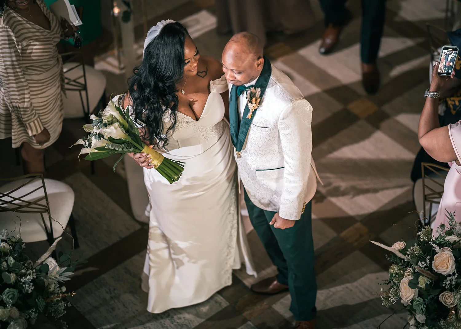 Tiffany and David walk together up the Palladian Hall aisle in their ceremony attire, smiling at each other.