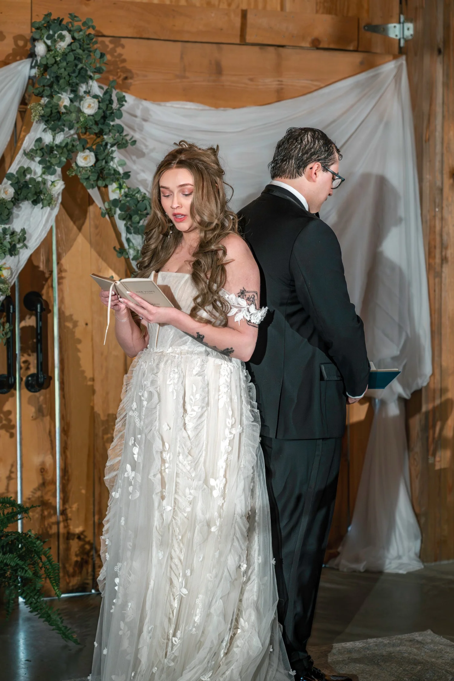 Lindsey reading her vows to Noah from a small book in front of the white drapes