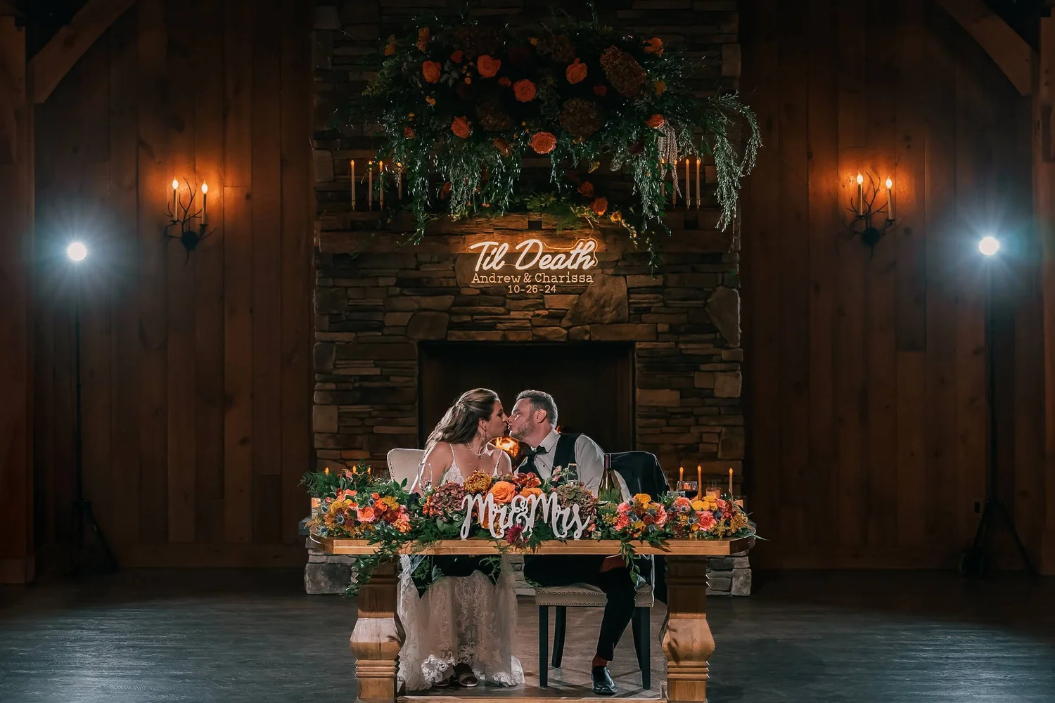 Charissa and Andrew kiss at their flower-lined sweetheart table inside Windham Manor