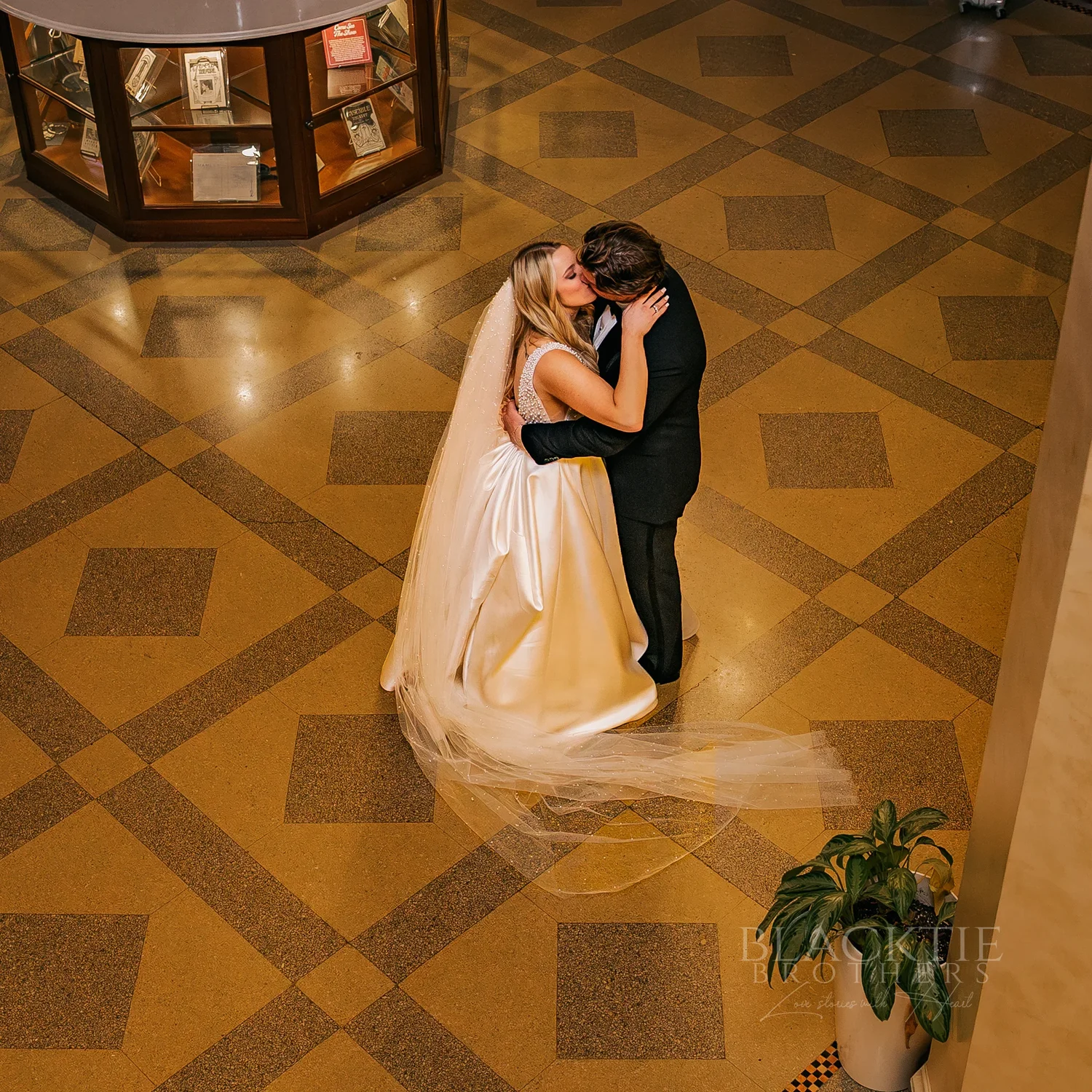 Catie and Brad kissing on the patterned lobby floor, photographed from above, at Marriott Syracuse Downtown