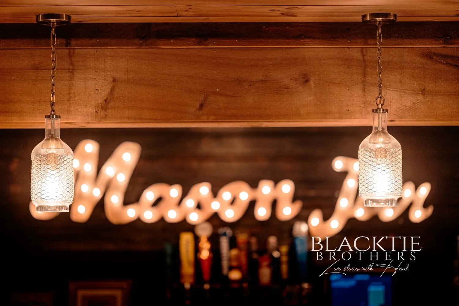 A lit marquee sign reading Mason Jar on a wood-panelled wall above the bar, with two glass pendant lights hanging in front of it