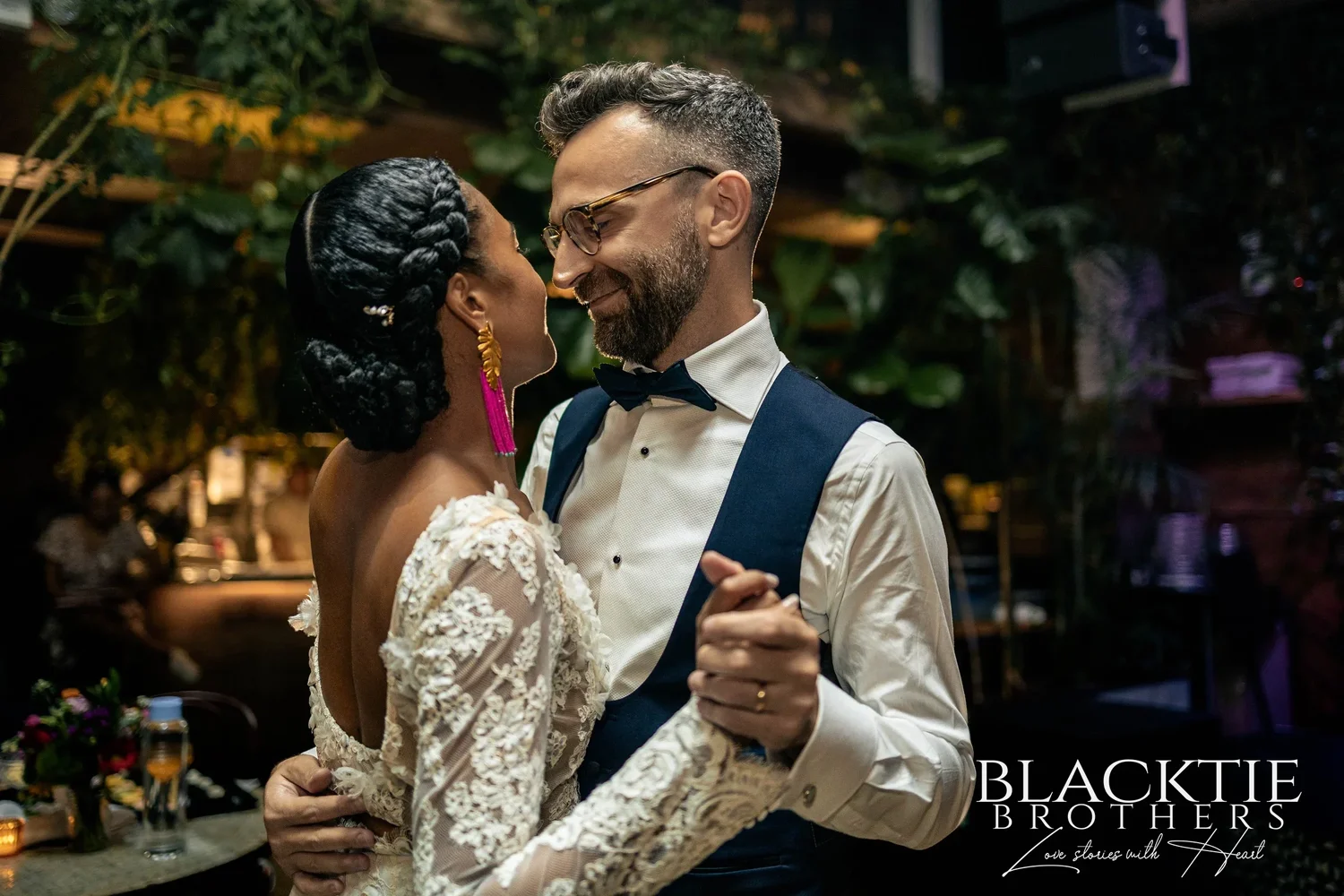 Ciara and Drew laughing nose to nose during their first dance, plants and warm lights behind them