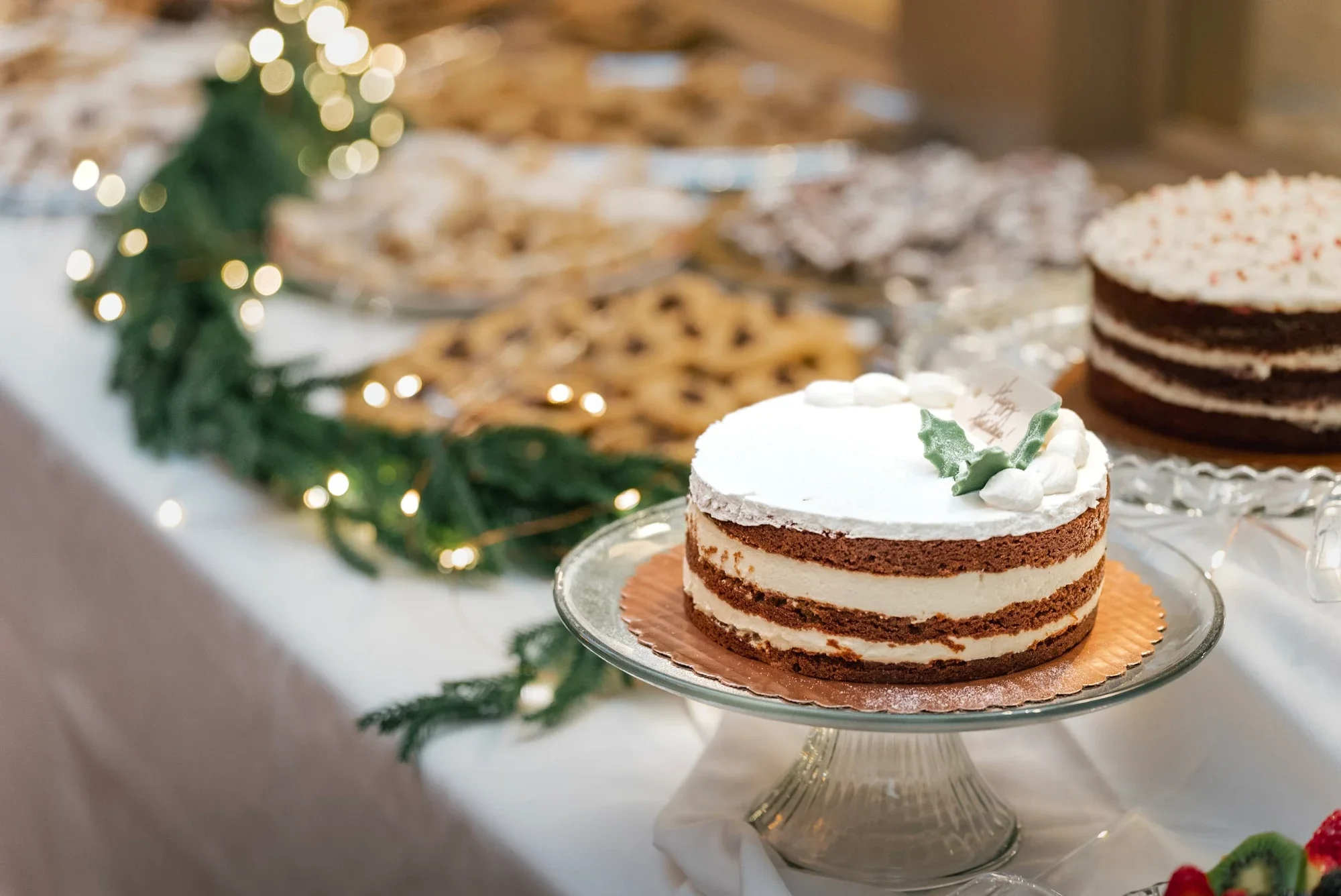A dessert table with layered cakes and cookies beside evergreen garland at Remlik’s.