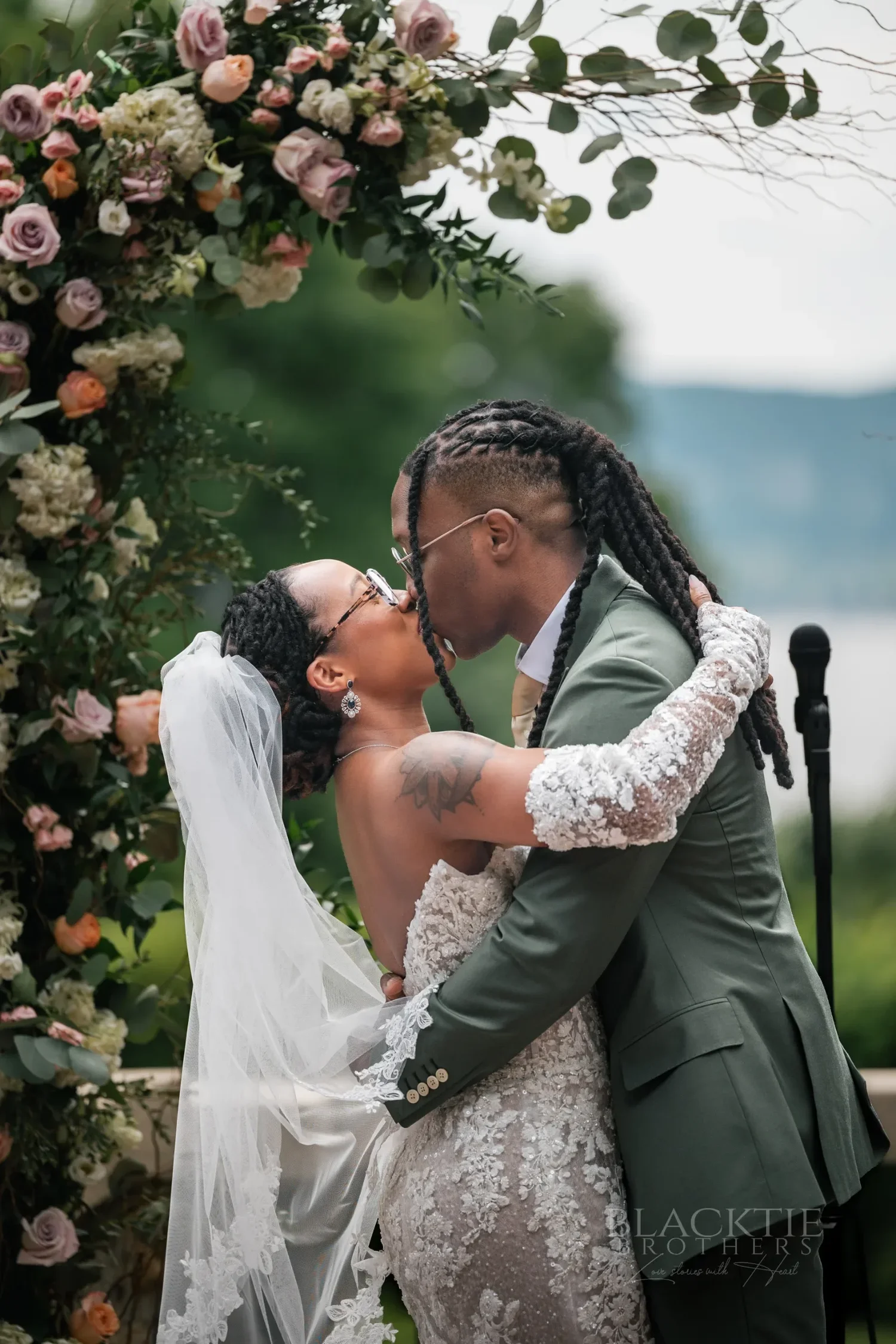 The couple kissing beside a floral arch, the Hudson River and hills behind them
