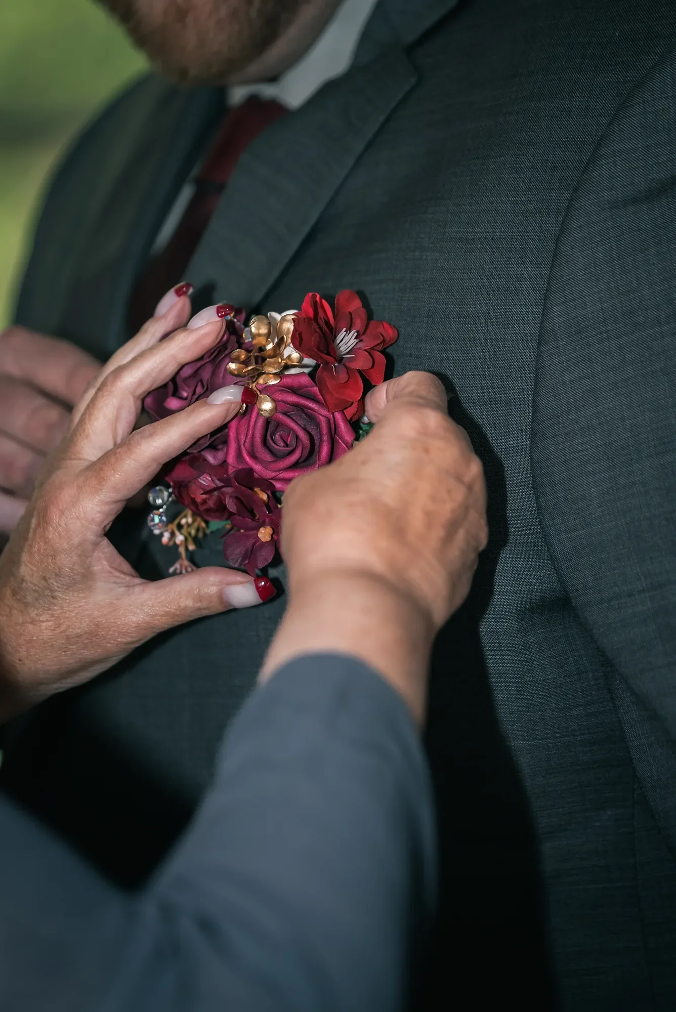 Burgundy boutonniere being pinned to a groom's suit at Stoney Creek Castle