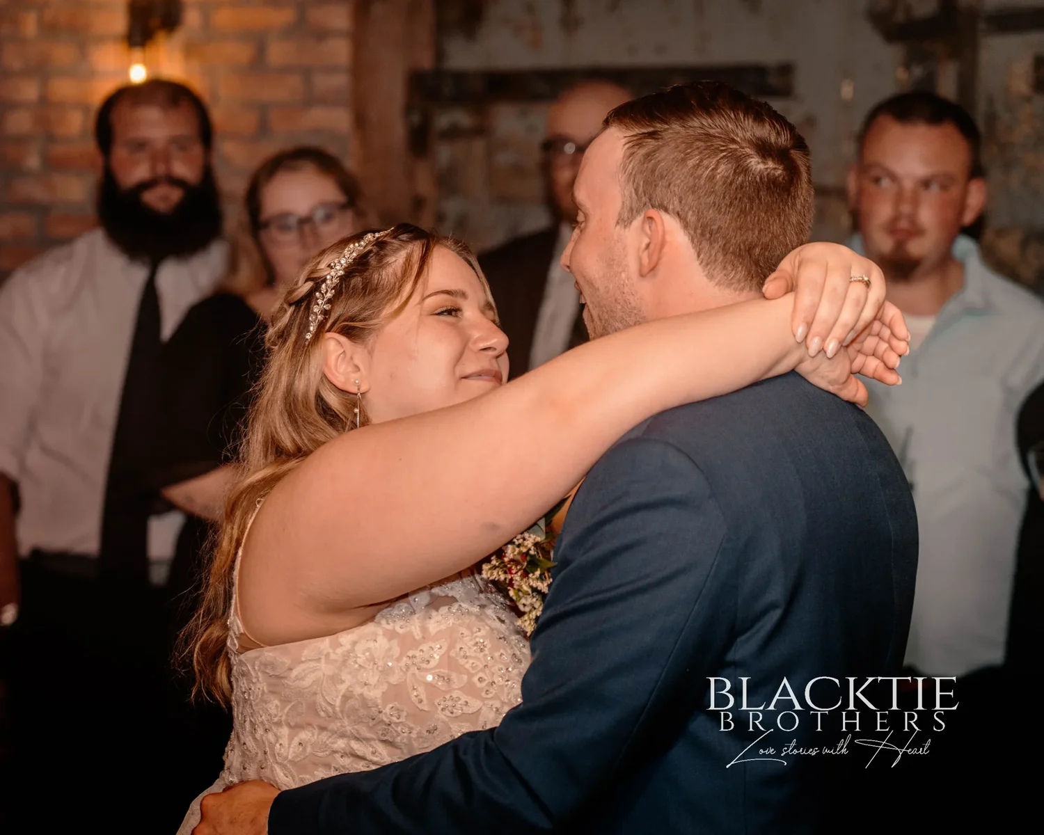 Jennifer and Jared's first dance, her arm around his neck, guests standing close around the small dance floor