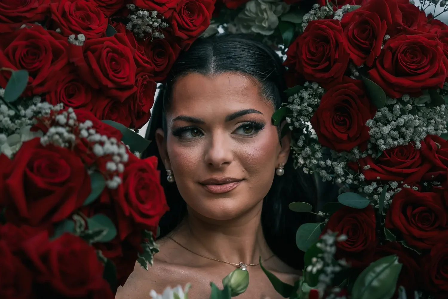 Vanessa framed by red roses on her wedding day at Turning Stone Resort Casino, photographed by BlackTie Brothers