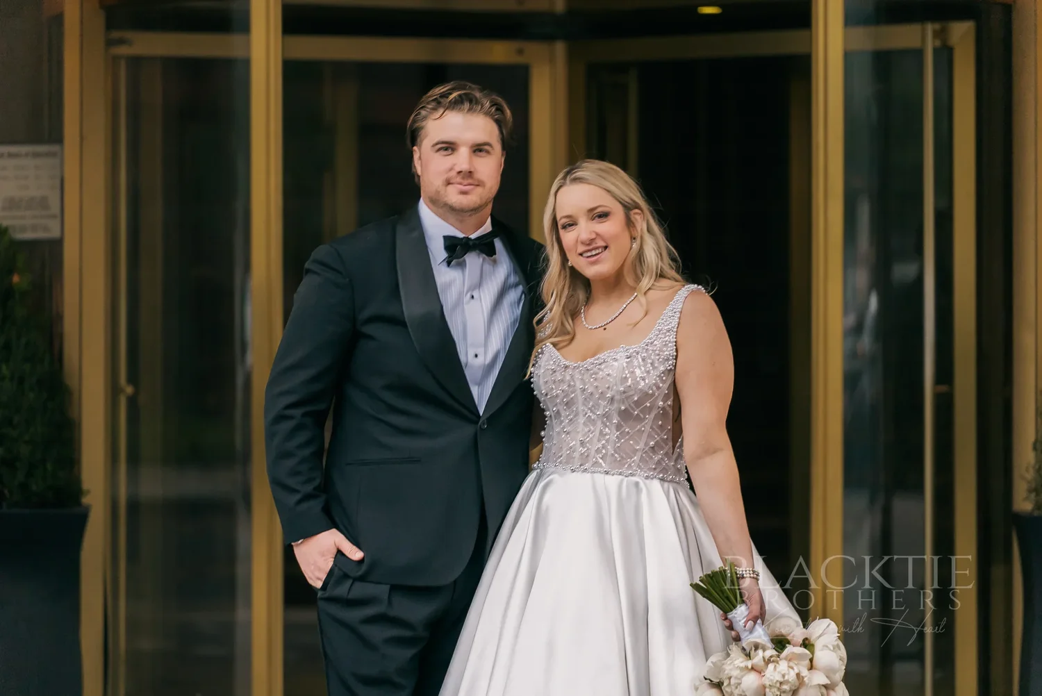 Catie and Brad smiling together in the brass doorway of Marriott Syracuse Downtown