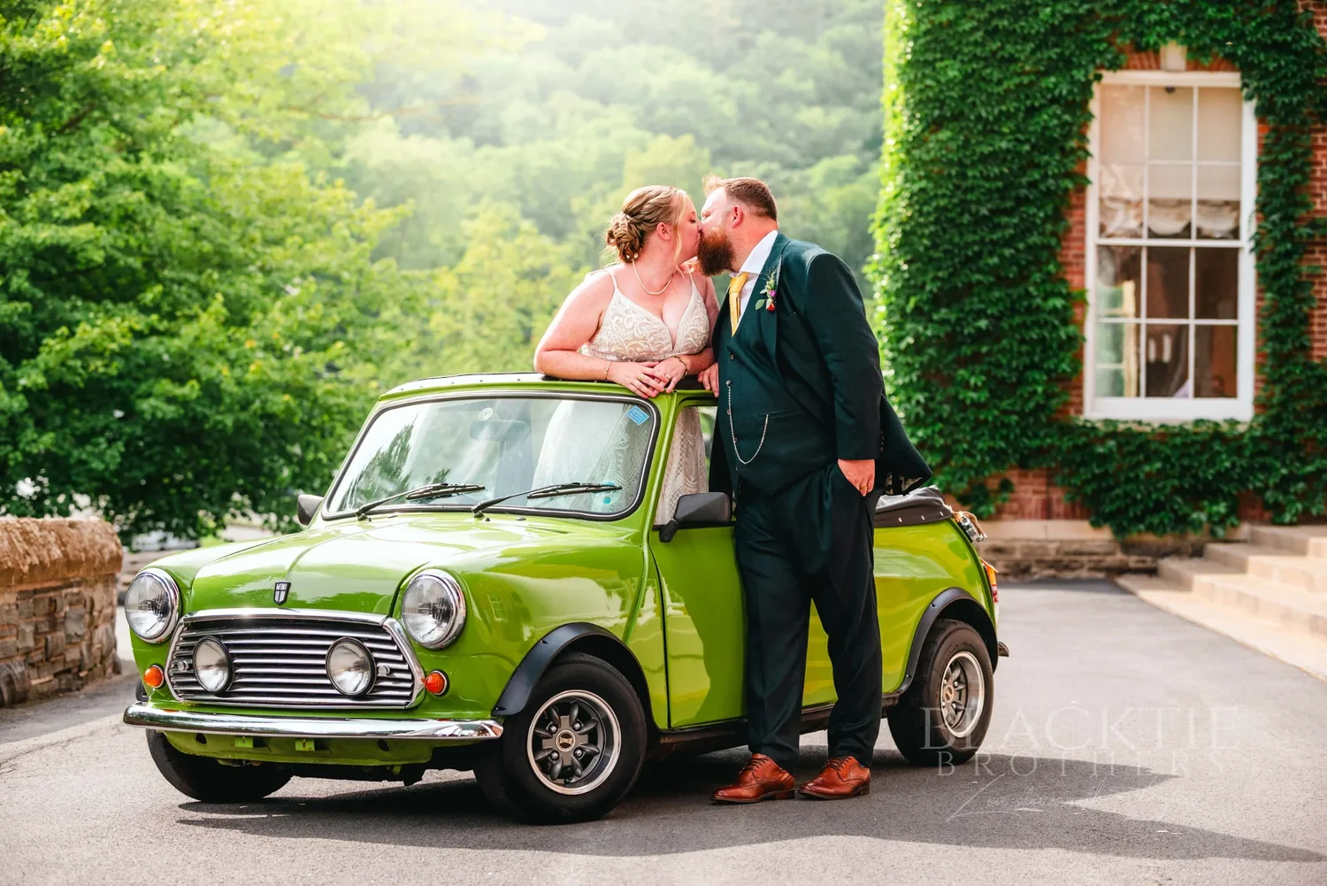 Amanda and Chris beside a green Mini Cooper by the ivy-covered wall at The Otesaga
