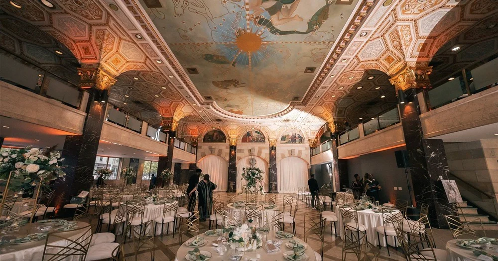 The ballroom at Palladian Hall in Syracuse, New York, with a painted ceiling, gilded columns and reception tables