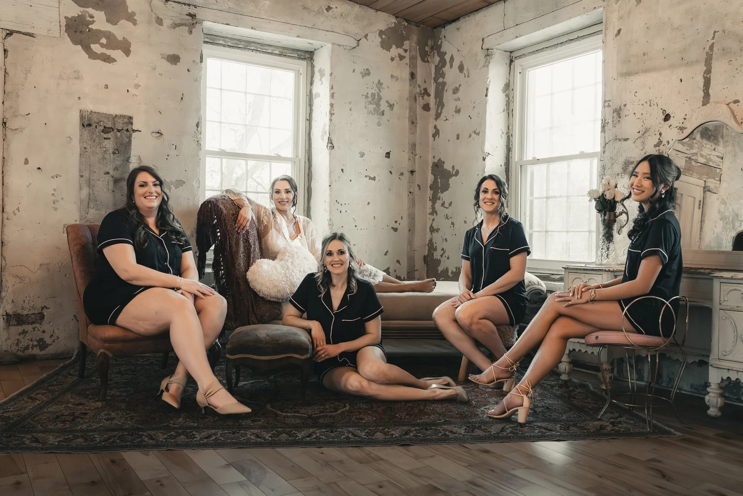 Jill and her wedding party seated together in a stone-walled room with tall windows at The Sinclair of Skaneateles