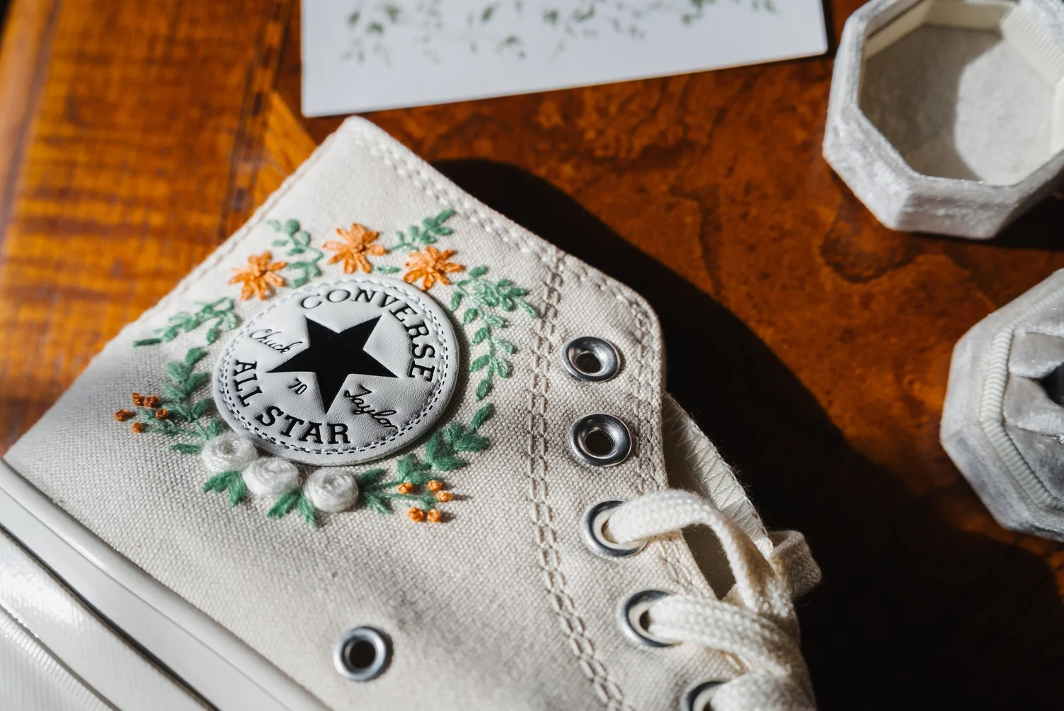 White Converse high-tops embroidered with orange and pink flowers, laid out before the wedding