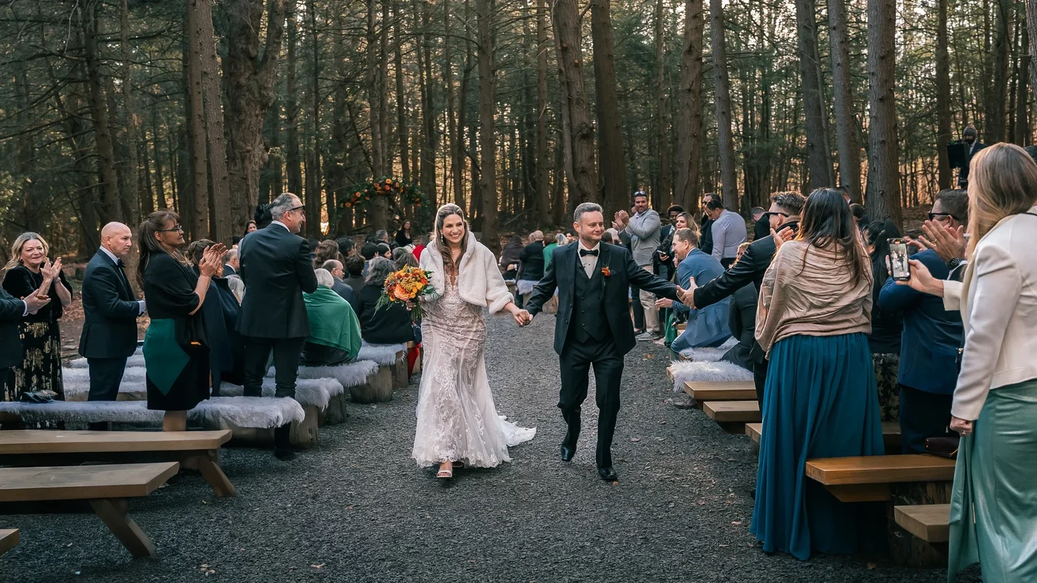 Charissa and Andrew walking back up the gravel aisle of the Enchanted Forest as guests stand and cheer on both sides