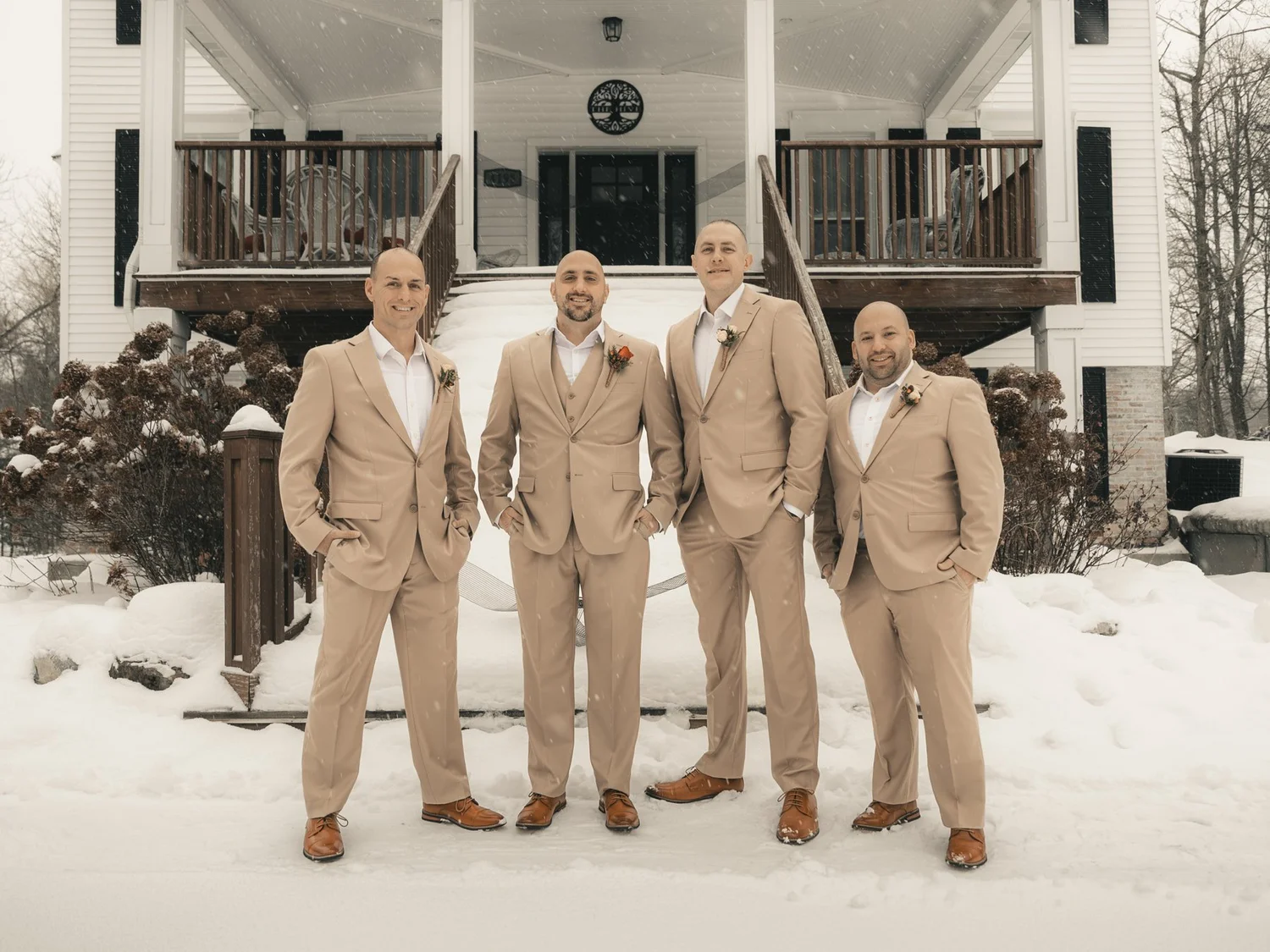 Nick and three members of his wedding party in tan suits standing in snow outside The Sinclair of Skaneateles