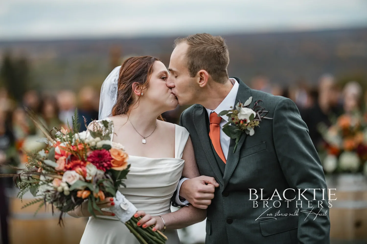 Anya and Gabe kissing in the aisle after the ceremony at Glenora, Anya holding a bouquet of copper and cream flowers