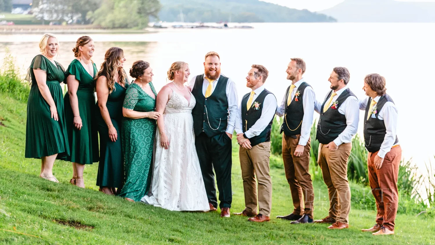 Wedding party in emerald dresses and green waistcoats on the lawn by Otsego Lake at The Otesaga