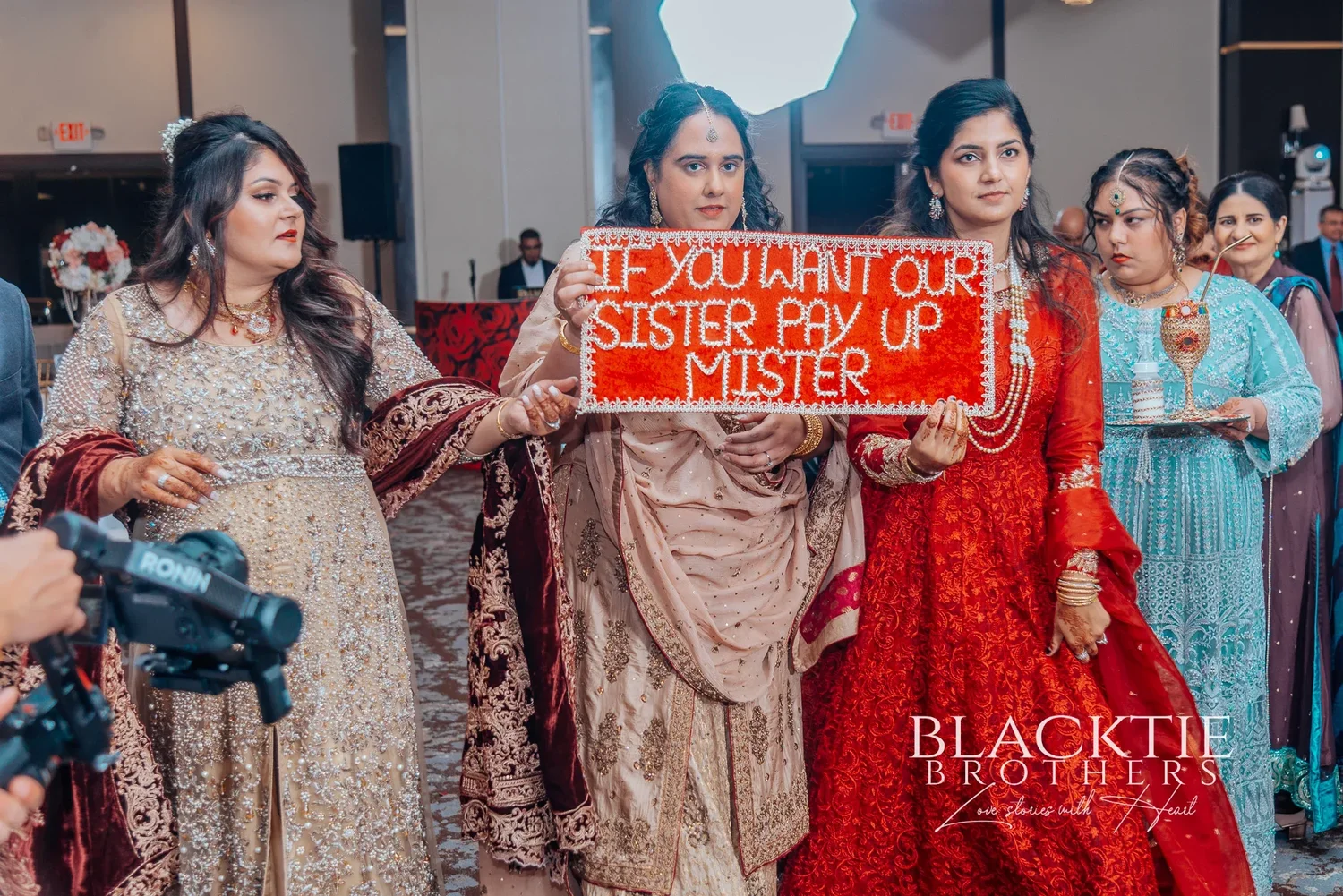 A group of women in embroidered outfits holding up a red sign that reads: If you want our sister pay up mister