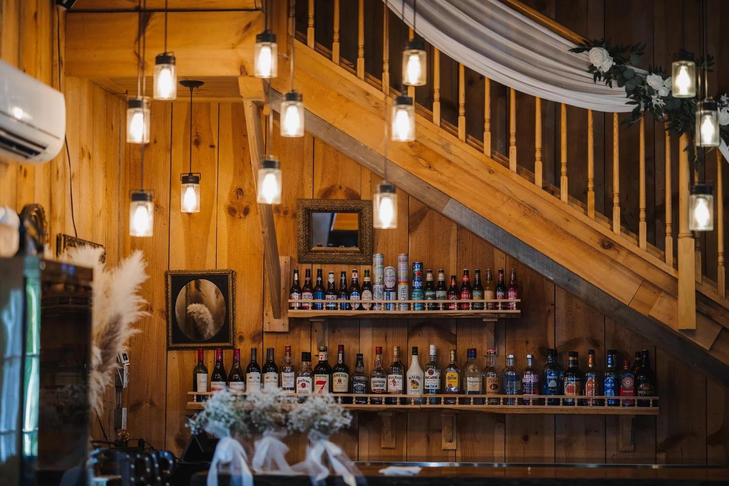 The wooden bar under the staircase in the Wolf Oak Acres barn, with hanging bulb lights and draped fabric