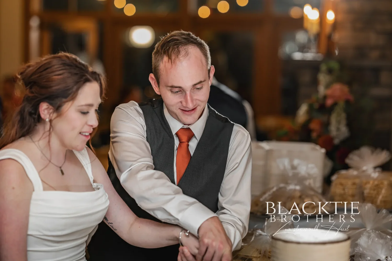 Anya and Gabe cutting their cake at the reception at Glenora, warm lights behind them
