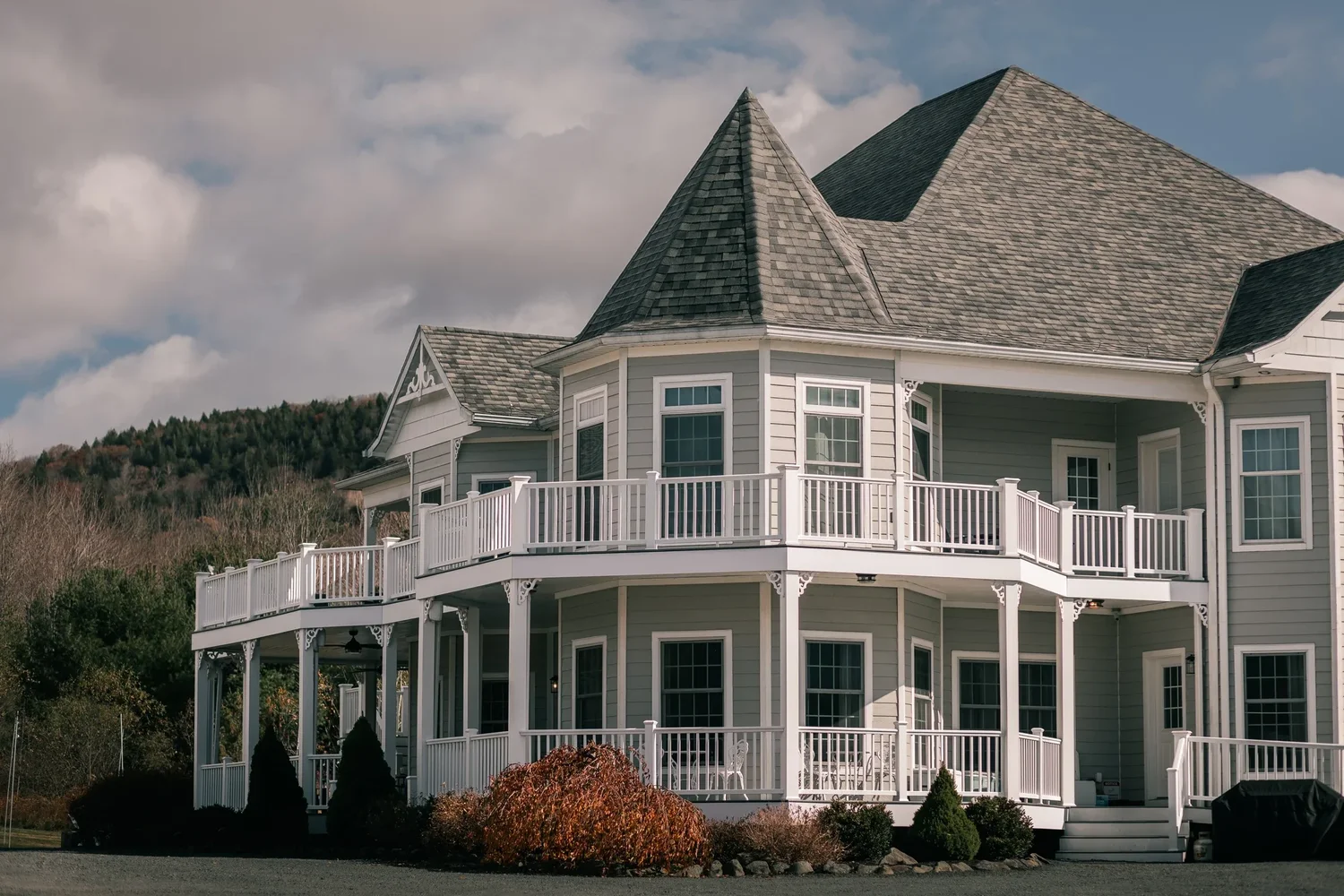The white Victorian Manor House at Windham Manor in daylight, with its turret, wraparound porch and upper balcony against the mountains