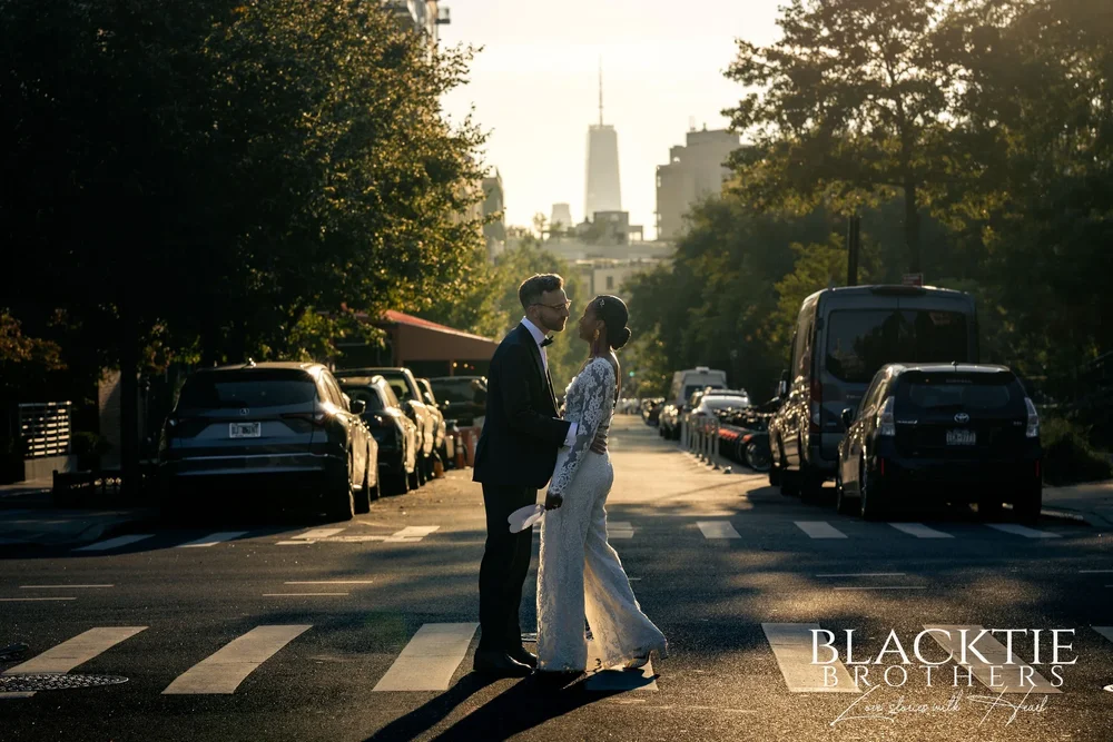 A couple face to face in a sunlit Brooklyn crosswalk, with One World Trade Center at the end of the street