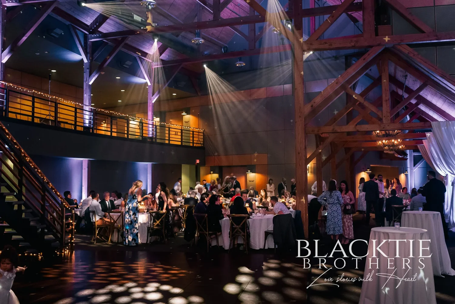 The great room at Allyn Lodge after dark, with purple uplighting on the timber posts and guests on the dance floor.