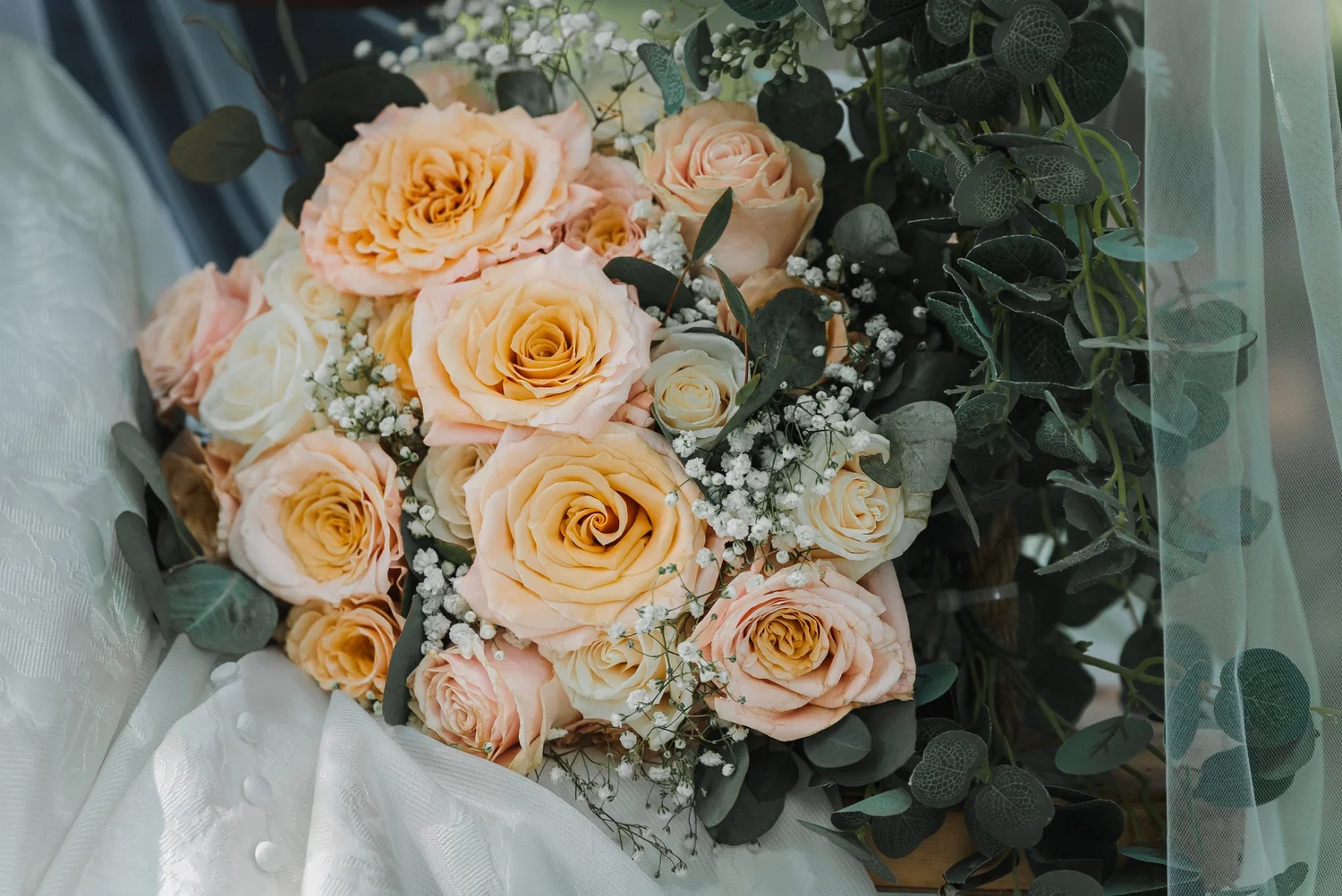 A bouquet of peach roses, baby’s breath and eucalyptus resting on a veil