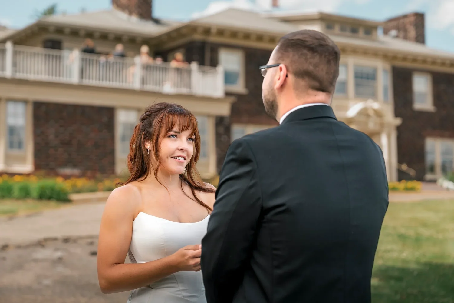 Danielle smiling at Zach during their first look on the lawn at Traditions at the Glen, the mansion behind them