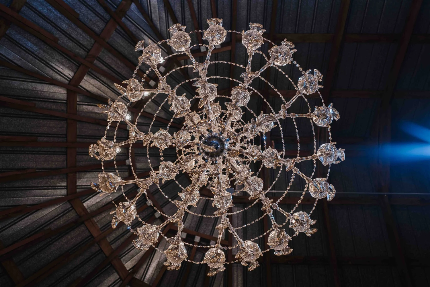 A crystal chandelier viewed from directly below against the barn's exposed wood ceiling.