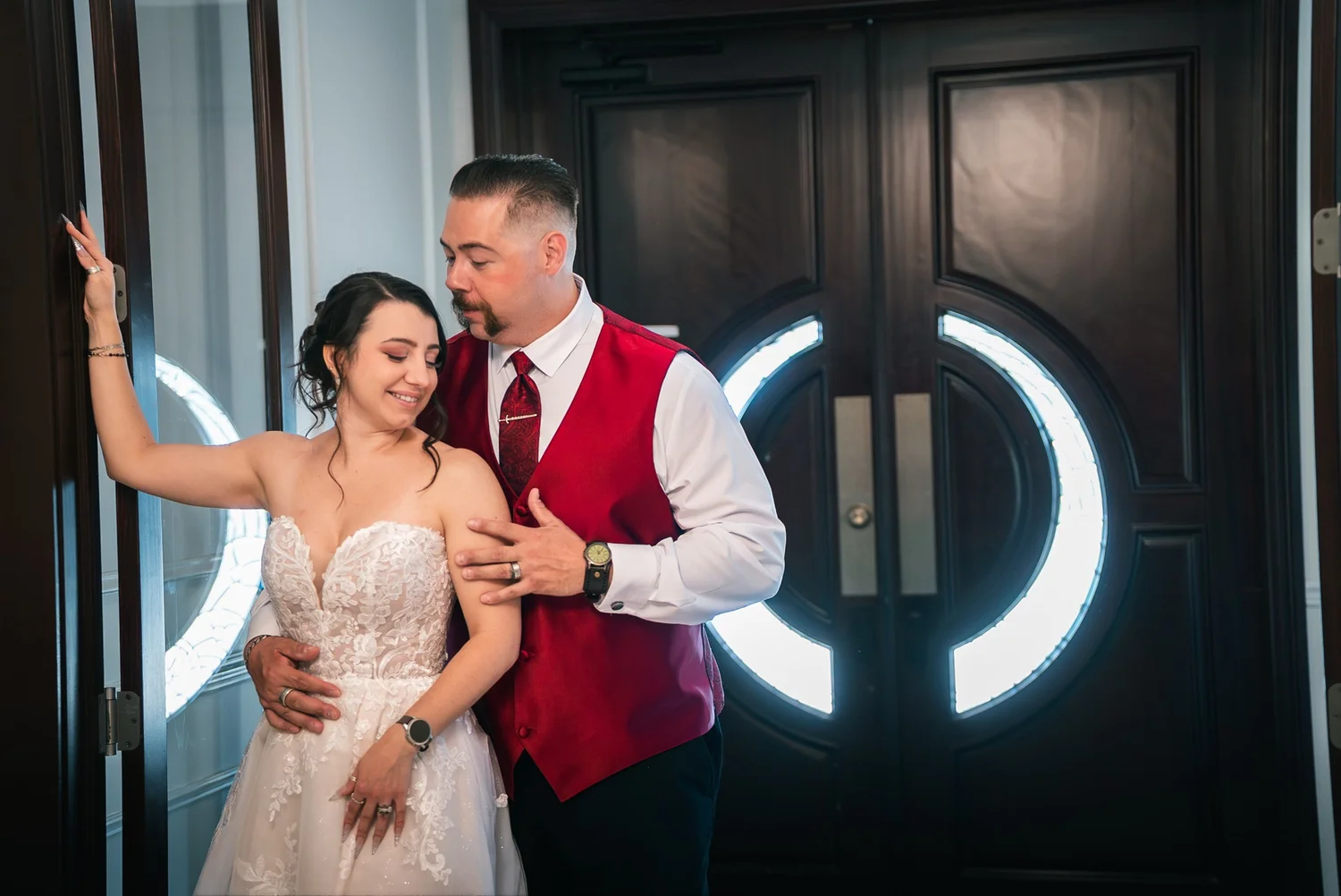 Laura and Dante laughing together in front of dark double doors with glowing circular lights