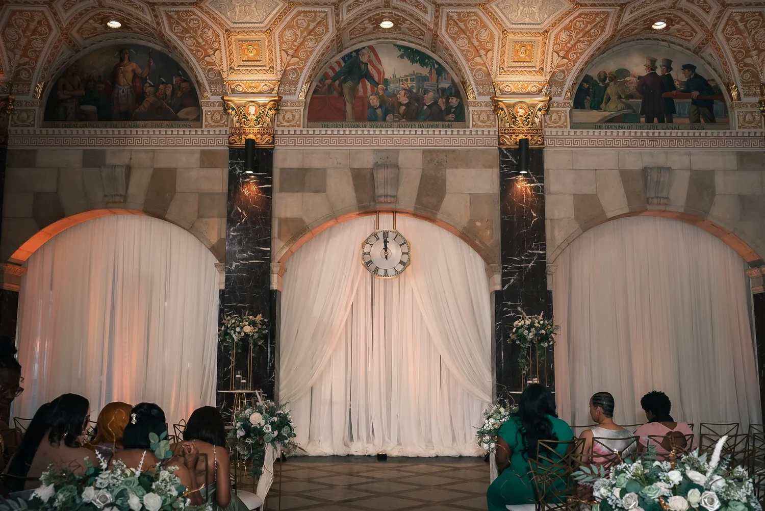 White ceremony draping and flowers beneath the ornate ceiling and marble columns at Palladian Hall.