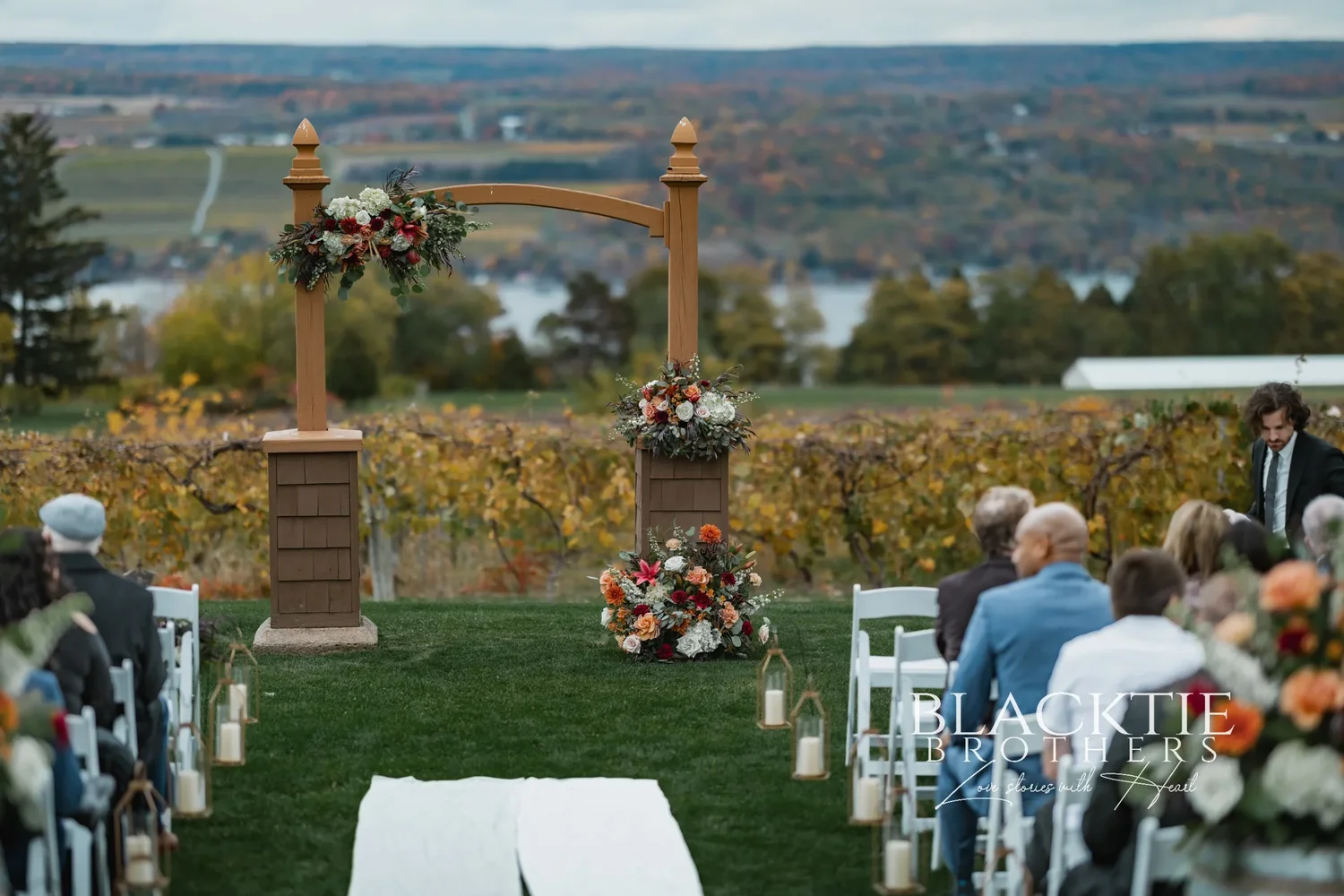 The wooden ceremony arbor at Glenora Wine Cellars dressed with autumn florals and candles before guests arrived, Seneca Lake in the distance