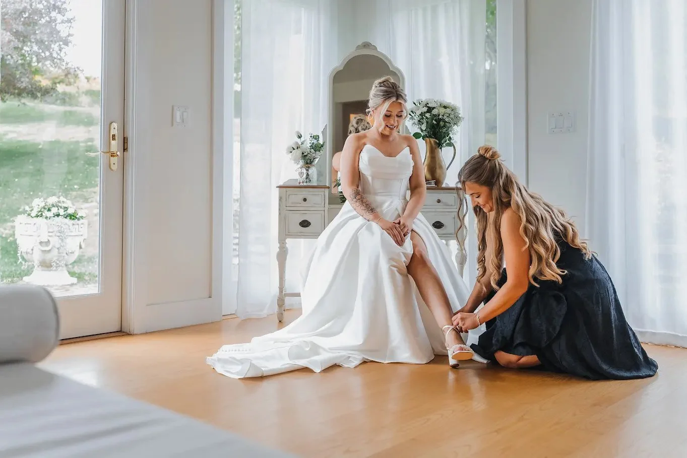 Bride receiving help with her shoes in a bright Stonewall Estate suite