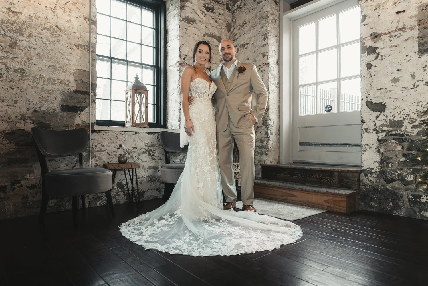 Jill and Nick standing together between tall windows and exposed stone walls at The Sinclair of Skaneateles