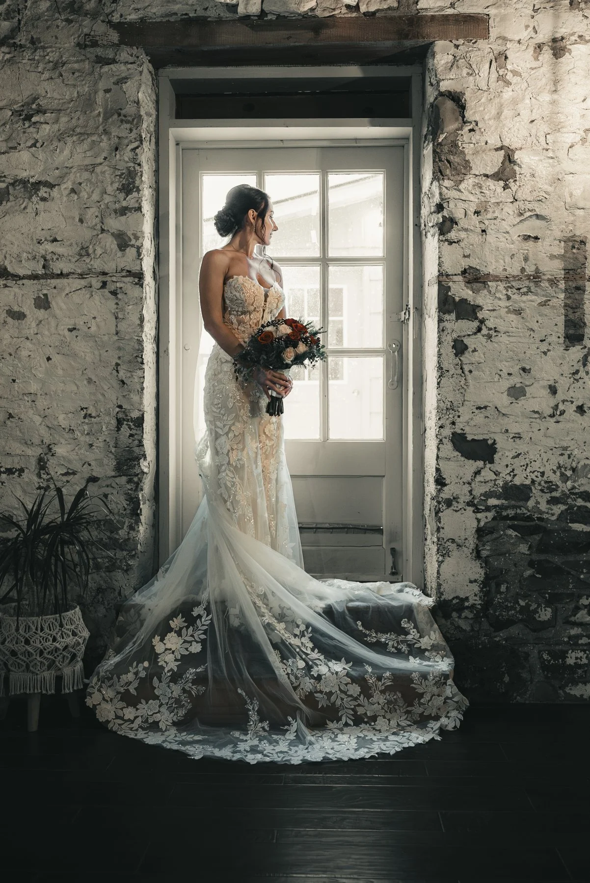 Jill in her lace wedding gown holding her bouquet beside a tall window at The Sinclair of Skaneateles