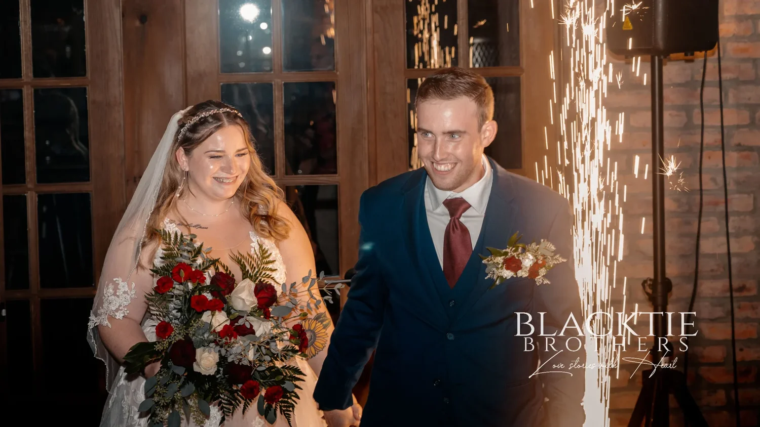 Jennifer and Jared entering the reception room through wooden doors as cold sparks shoot up beside them, brick walls behind
