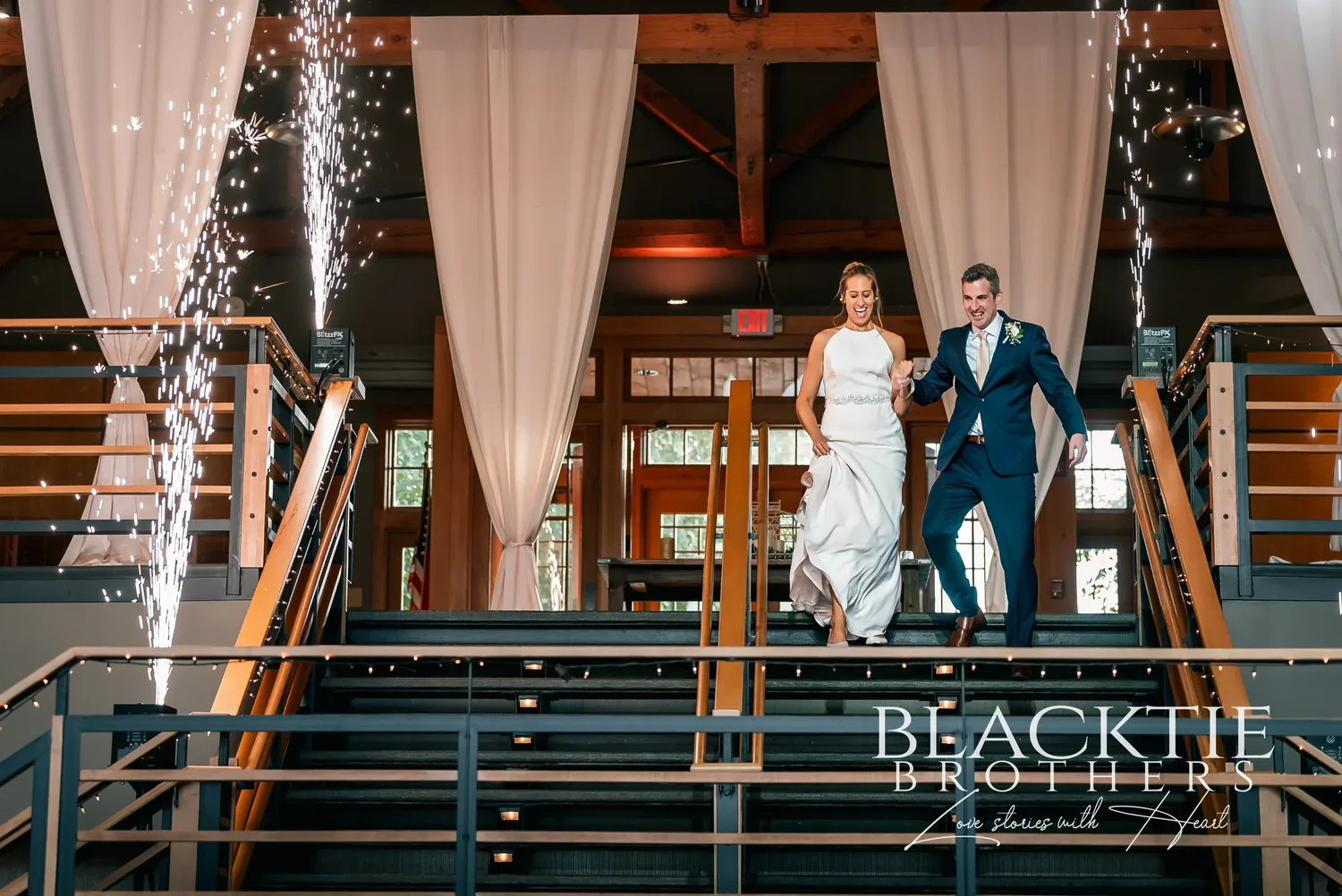 A couple making their entrance down the mezzanine staircase inside Allyn Lodge with spark fountains on either side.