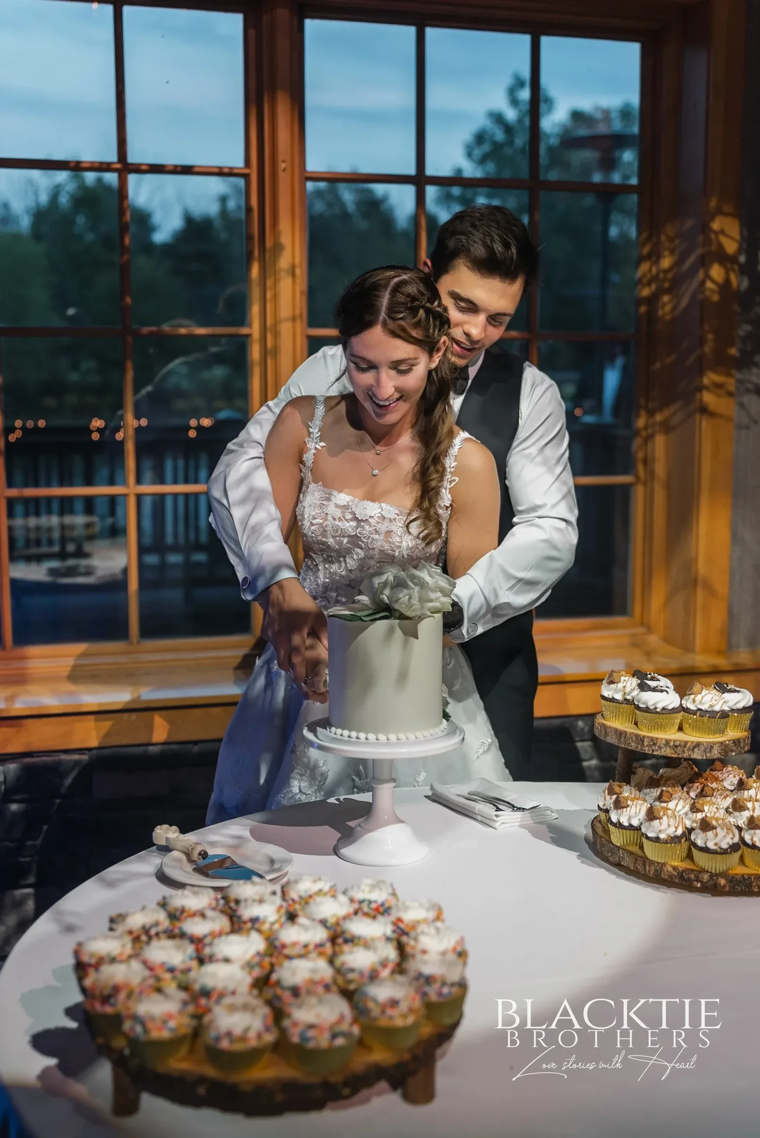 A couple cutting their cake at the window wall inside Allyn Lodge.