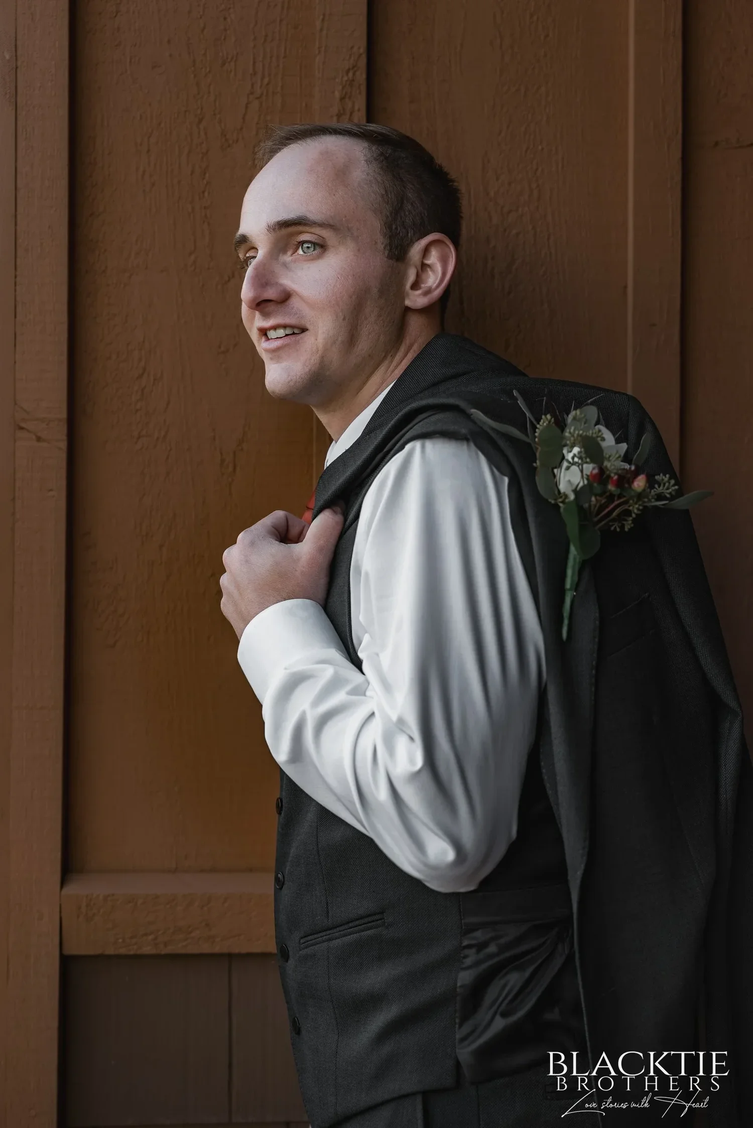 Gabe at The Inn at Glenora with his jacket over his shoulder and a boutonniere pinned to it, lit by the window