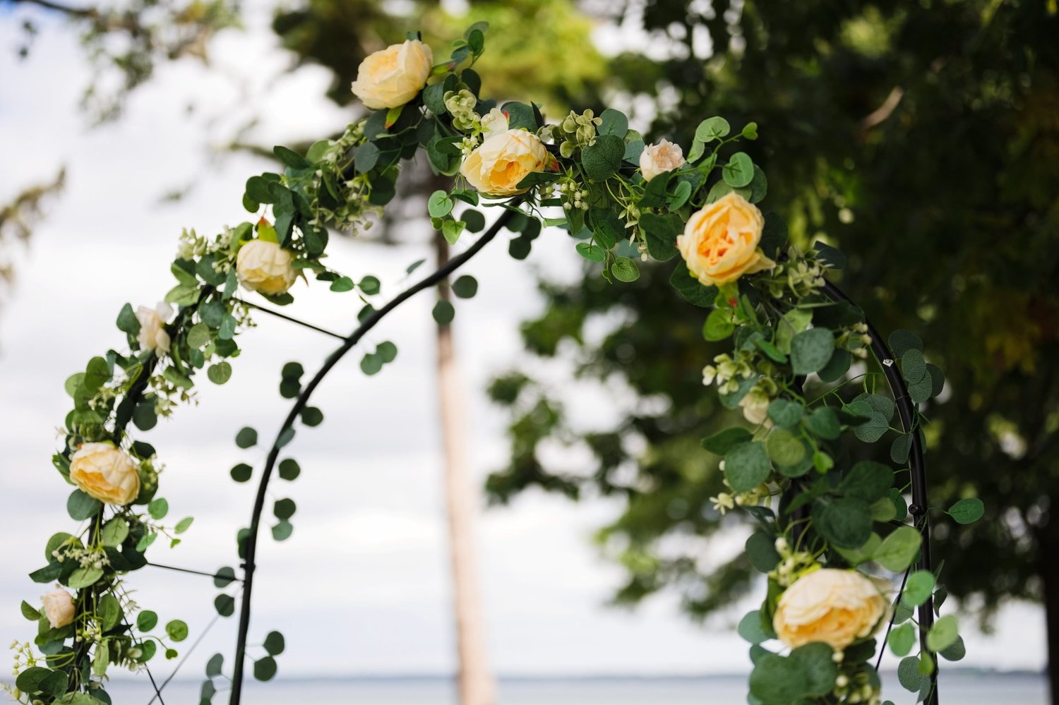 Yellow roses and greenery wound around the ceremony arch, with Seneca Lake soft in the background
